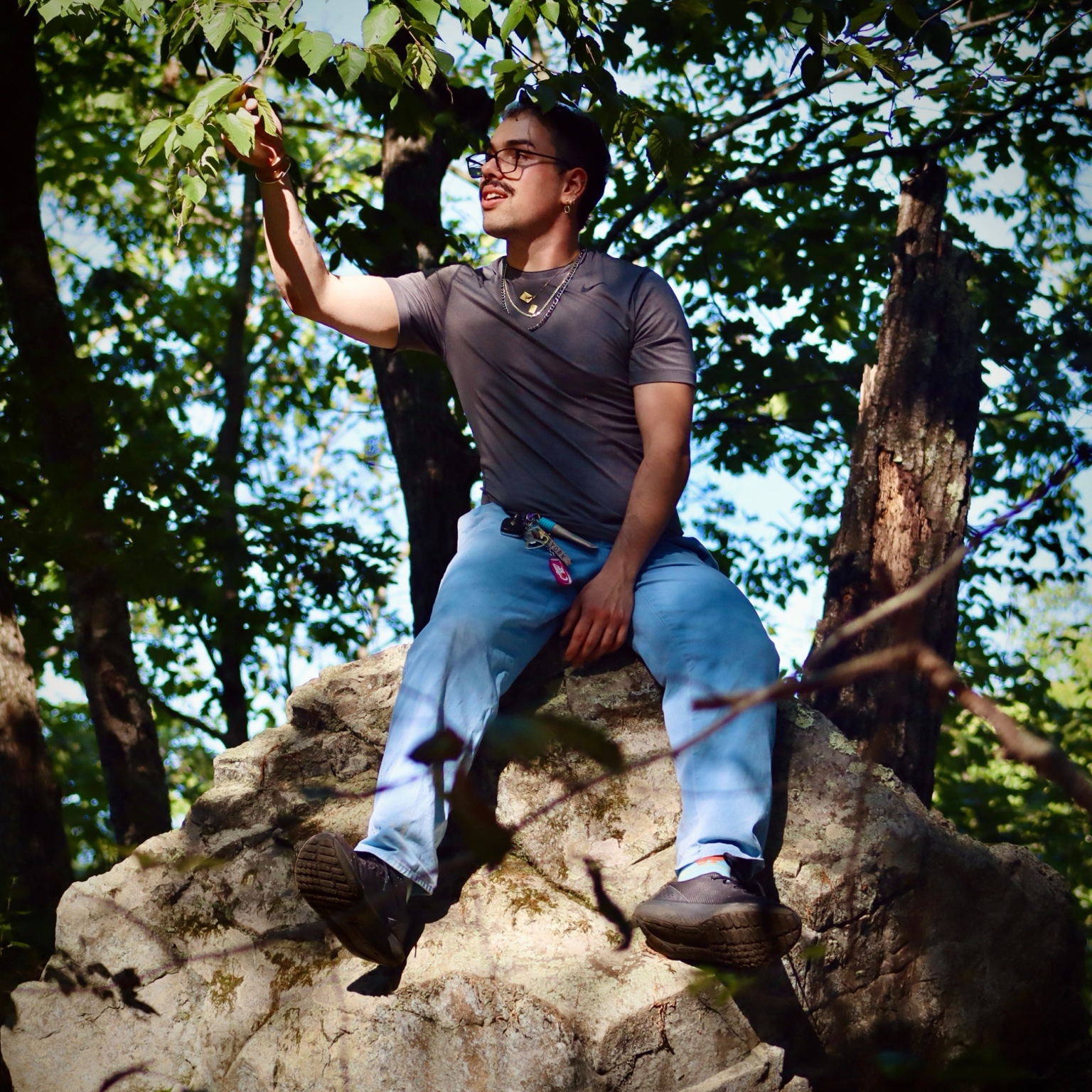 Blake Lee sitting on a rock beneath leafy trees